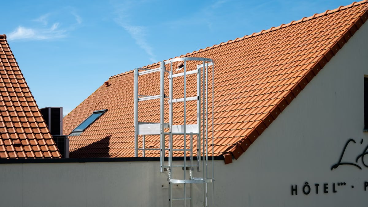 Sunny view of a hotel rooftop with ladder, featuring terracotta tiles and blue sky in Escalles, France.